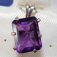 Close-up of rectangular faceted amethyst gemstone pendant in sterling silver setting showing prongs and bail.