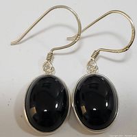 Front view of sterling silver earrings with polished oval black onyx stones set in bezels and hanging from textured hooks.