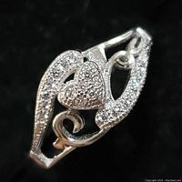 Close-up view of sterling silver ring, showing heart shape with CZ stones and decorative open swirls also studded with CZ stones.