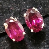 Close-up photo of a pair of sterling silver earrings each holding an oval faceted garnet gemstone in four-prong settings.