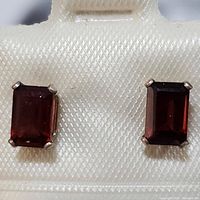 Close-up front view of both rectangular garnet sterling silver stud earrings in a textured display box