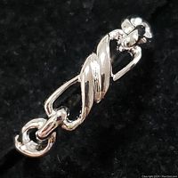 Close-up photo of sterling silver ring showing twisted and linked loops design on a black background.