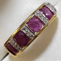 Close-up image of the top and side of the gold-toned sterling silver ring showing oval and round ruby stones separated by clear stone bars.
