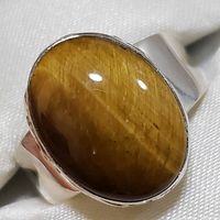 Close-up image of the polished oval tiger eye gemstone set in sterling silver ring, showing chatoyance and smooth band finish.