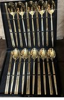 Full view of the set with 10 spoons and 20 chopsticks held in the display case showing the gold-tone reflective utensils with decorative etched handles.