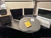 Wide view of four laptops, Panasonic monitor, TomTom GPS, Vonage box, laptop pillow and Vistablet on a black surface