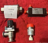 Top down view of the four valves arranged on red quilted surface showing various shapes and fittings including branded labels
