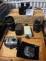 Overview of camera, lenses, binoculars, slide viewer and small camera accessories arranged in wooden box