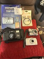 Photo showing Olympus Trip 600 camera in original package, Pentax 105WR camera, Olympus FE 10 camera, Nikon Coolpix waterproof camera and RMC Tokina 58mm lens filter.