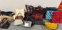 Wide shot showing 18 assorted purses and totes arranged against wall on floor