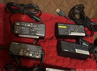 Five black Lenovo laptop AC power adapters with labels visible showing certification and power ratings. Two adapters have 65W output, three have 45W output with slim tip connectors and power cords bundled with velcro straps.