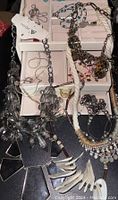 Photo of various vintage necklaces arranged on and around two light pink jewelry boxes, showing different styles including beaded, rope, rhinestone, and animal print necklaces.