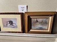 Two framed Native American themed paintings side by side, one featuring teepees in snow, the other a resting figure.