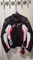Front view of Alpinestars motorcycle jacket in black, white and red with tags attached.