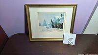 Framed print on a table with a lot number card showing the artwork titled 'Christmas on Main Street' with visible light snow scene.