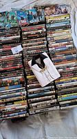 Top view of over 100 DVDs arranged in rows, including cases and some DVDs in sleeves, with a decorative fabric shirt placed on top.