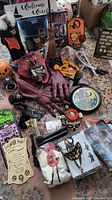 Photo shows a large red demon mask with hands, pumpkin-headed decorations, various Halloween signs, a clock, boxed costume masks, plastic guns, and small prop items like candles and eyes scattered on floor.