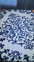 Close-up photo showing cream or beige colored flat woven rug with dark blue ornate scroll and floral decorative pattern.