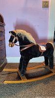 Side view of black plush rocking horse with cream mane and wooden rockers, showing leather tack details
