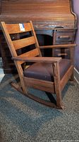 Side view of solid wood rocking chair with brown cushioned seat, showing armrests and rocker base.