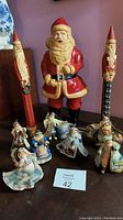 Photo showing the full collection including vintage blow mold Santa in the center, tall carved wood Santas on sides, and various Thomas Kinkade Old World Santa ornaments in front.