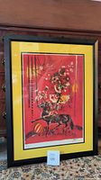 Framed wall art with a black frame and yellow matting, featuring a red and black abstract image with horse and geometric shapes.