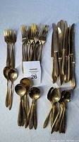 Full set of solid brass utensils including forks, spoons, and knives on a blue background.