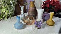 Overview of all 8 assorted vases and decorative glass items arranged on table.