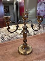 Side angle view of the vintage three-arm brass candelabra placed on a granite countertop, showing its overall shape and design.