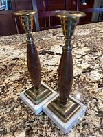Pair of vintage candlestick holders made with wood, brass, and marble placed on a granite countertop, showing front view.