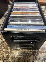Black leather file holder filled with various music CDs, showing a stack from side view.