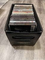 Photo of black leather file folder containing stacked music CDs showing titles of several albums