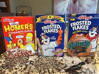 Three Kellogg's cereal boxes standing upright on countertop: The Simpsons Homer's Cinnamon Donut (2001), Frosted Flakes Toronto Blue Jays (1992), Frosted Flakes Vancouver Grizzlies (1994)
