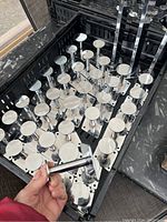 Photo showing multiple round stainless steel wall hooks with square mounting base with 4 screw holes, grouped in a container.