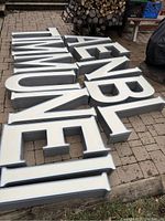 Exterior light up sign letters laid out on outdoor ground surface, showing metal framing and white faces of letters.