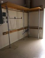 Installed shelving system showing chrome upright posts supporting wooden shelves and hanging rails mounted on wall brackets.