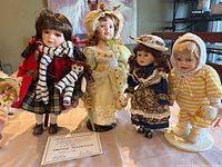 Four standing porcelain dolls displayed together on a table, including certificate of authenticity.