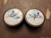 Two hockey pucks on a wooden surface, each with a Great Blue Heron Charity Casino label and John Tavares autograph including his number #91 in ink.