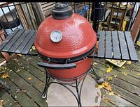 Front view of red ceramic grill on cart with folding shelves and thermometer