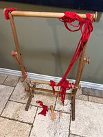 Full view of wooden Ram loom with red yarn and tools on tiled floor
