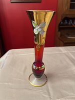 Front view showing white hand painted flower on gold flared top of Murano glass vase with red body and clear base