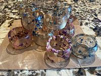 Overview photo showing all 12 transparent resin napkin holders arranged together, with embedded pink and blue wildflowers visible inside each napkin ring.