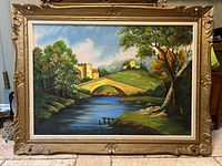 Full view of framed oil painting showing river, bridge, trees, hills, and buildings under partly cloudy sky.