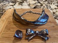 Top view of the three items: collar necklace, bow pin, and clip-on earring arranged on a wooden surface.