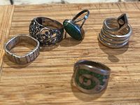 Set of five silver rings displayed on a wooden surface showing different styles and designs.