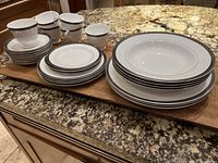 Full set of Spode Odyssey Black china arranged on a wooden surface, showing all plates, bowls, cups and saucers.
