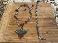Silver necklace featuring labradorite pendant and carnelian accents alongside a silver Mexican bracelet with wave design on a wooden surface.