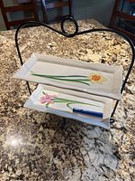 Front angle showing the two-tier ceramic trays with floral designs on black wrought iron frame on granite countertop