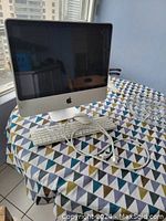 Front view of Apple 20-inch iMac on a table with Apple wired keyboard, wired mouse, and power cable laid out in front.