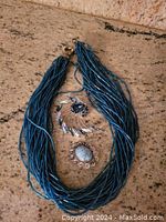 Photo showing the entire lot with blue beaded multi-strand necklace and two brooches on a stone surface.